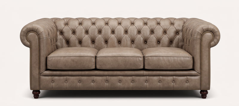 A classic Chesterfield loveseat sofa upholstered in taupe leather, featuring deep button tufting on the backrest and seat, rolled arms, nailhead trim, and dark wooden legs, shown against a plain white background.