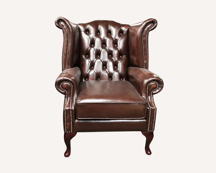 A classic brown leather wingback armchair with button tufting on the backrest, rolled arms, and dark wooden legs, shown against a plain white background.